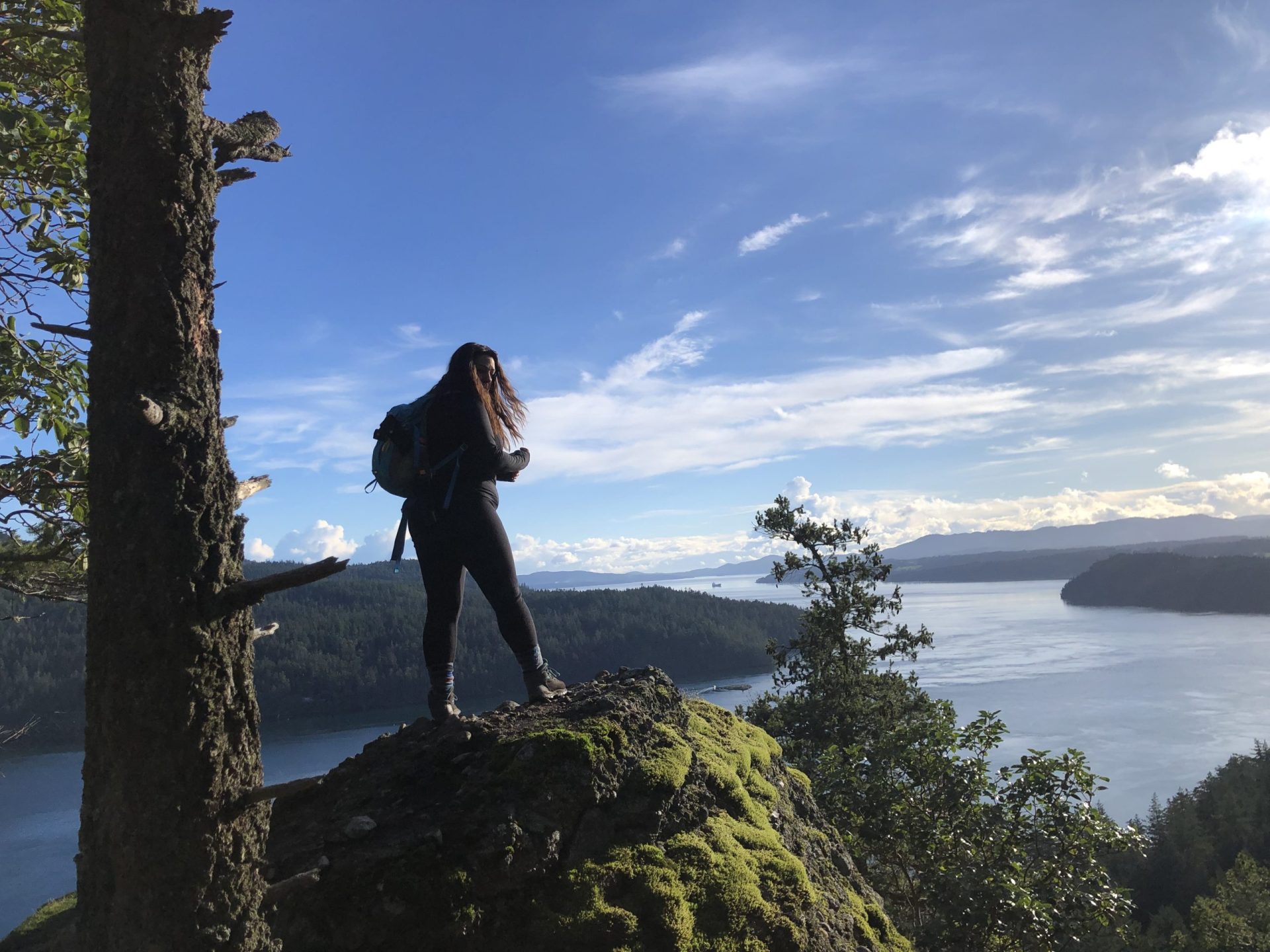 Hiker on a mossy bluff overlooking ocean inlets and forested islands on Vancouver Island